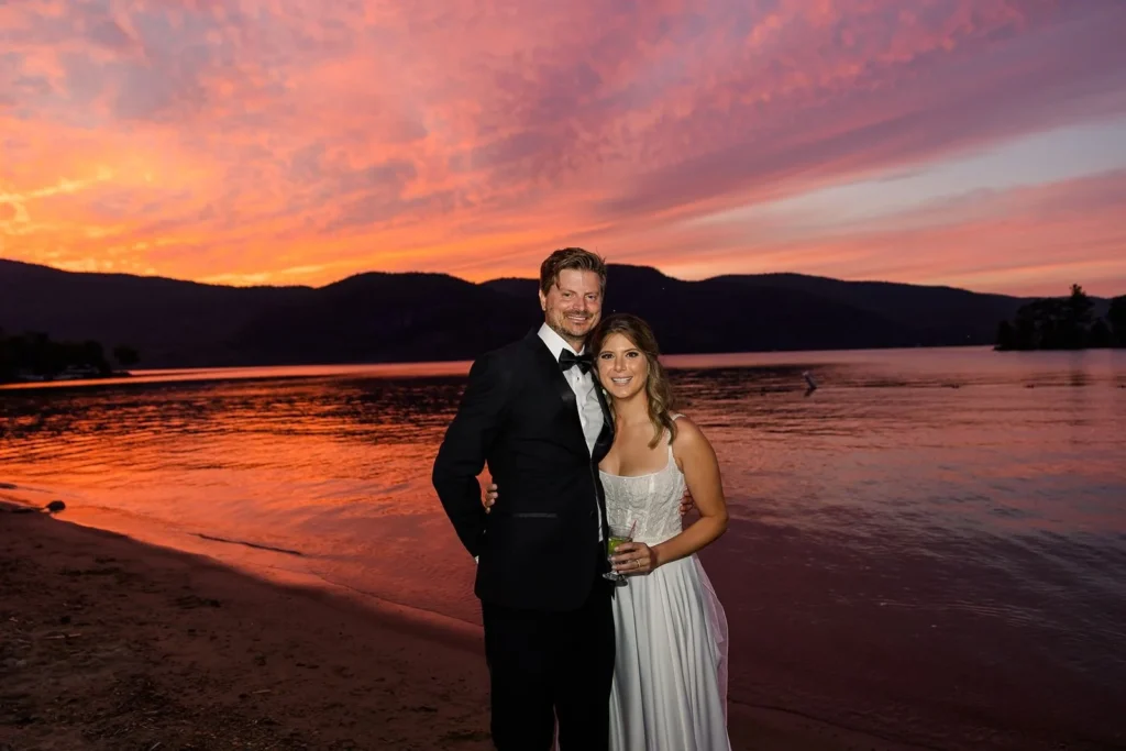 bride and groom smiling at camera with sunset behind them at Lake George, NY